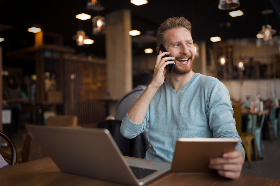 Young happy man having phone call in cafe